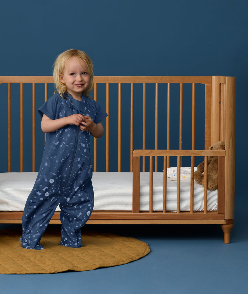 Toddler wearing an ergoPouch Sleep Suit Sack 1.0 TOG Starbeam, a sleeping bag that converts to a sleep suit with legs.