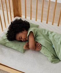 Toddler sleeping in a crib, resting on the ergoPouch toddler pillow case in Willow