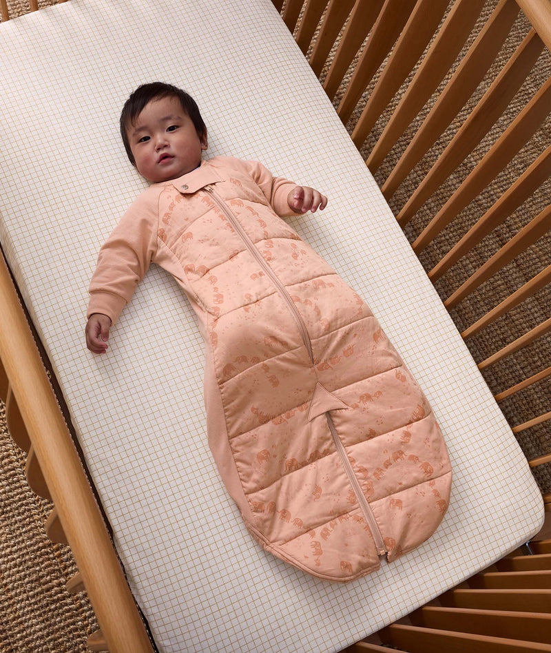 A baby lying in a wooden crib wearing a 2.5 TOG sleep suit sack with long sleeves.