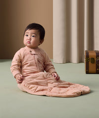 A baby sitting on the floor wearing ergoPouch Sleep Suit Sack with long sleeves and a front zipper. 