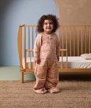 A toddler dressed in a 2.5 TOG Sleep Suit Sack stands next to a toddler bed.