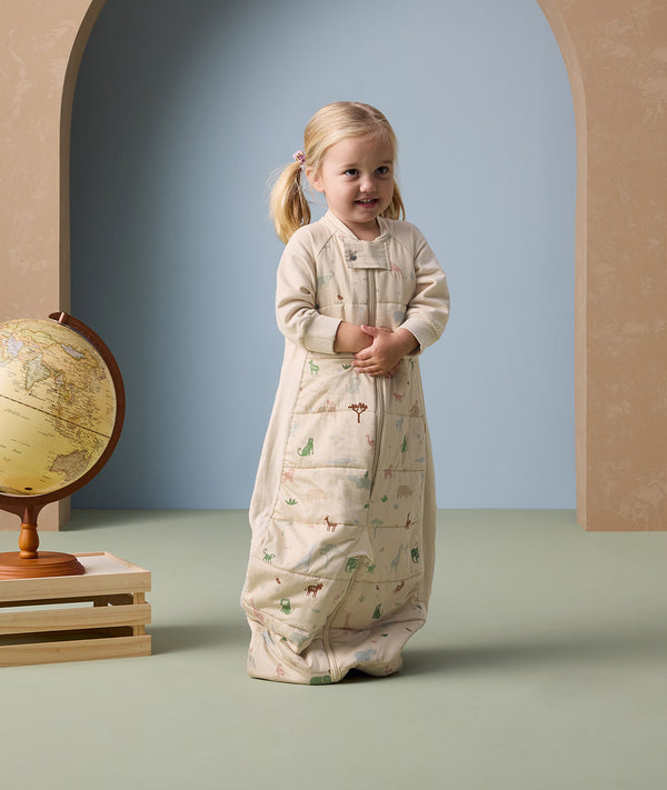 A toddler stands wearing an ergoPouch Sleep Suit Sack 2.5 TOG in bag mode.