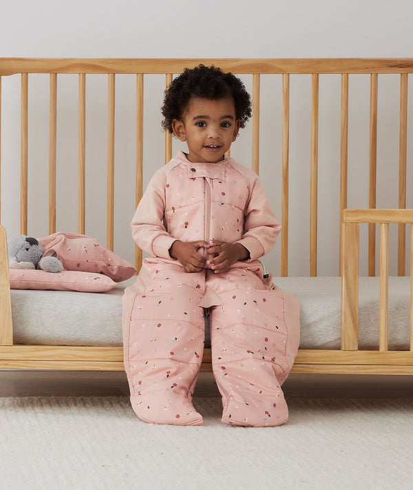 Child sitting in an ergoPouch Sleep Suit Sack 2.5 TOG Daisies, a warm sleeping bag that converts to a sleeping bag with legs