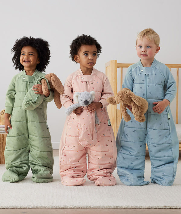 Three children standing in an ergoPouch Sleep Suit Sack 2.5 TOG Willow, Daisies and Dragonflies, a warm sleeping bag that converts to a sleeping bag with legs