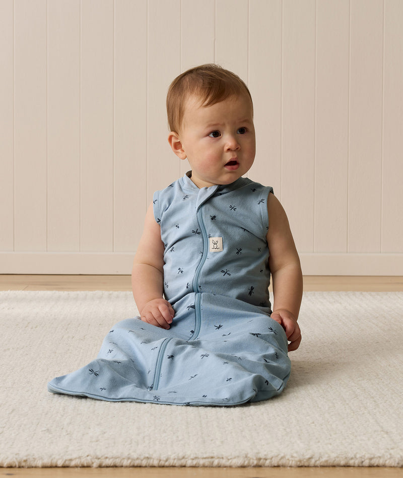 Infant wearing an ergoPouch Sleep Sack 0.2 TOG Dragonflies, sitting on a white mat