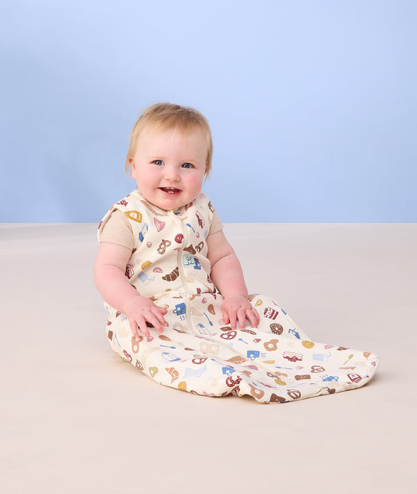 Infant baby sitting on the floor smiling wearing ergoPouch Sleep Sack 0.2 TOG in Bon Appetit