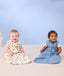 Two infants sitting on the floor wearing ergoPouch Sleep Sack 0.2 TOG in Bon Appetit and Petite Pretzel