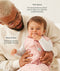 A dad holding a baby wearing a pink, patterned sleep sack over a long-sleeved romper with text highlighting TOG rating feature and wash & wear care.