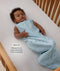 Infant lying on their back inside a wooden crib wearing a sleeveless dragonfly-patterned Sleep Sack with text highlighting slim-fit design for  an easy transition from swaddling.