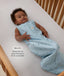 Infant lying on their back inside a wooden crib wearing a sleeveless dragonfly-patterned Sleep Sack with text highlighting slim-fit design for  an easy transition from swaddling.