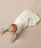 Baby crawling on a plain surface while wearing an oatmeal-colored sleep sack over a green long sleeved romper.