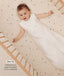 Infant lying in a wooden crib wearing a sleeveless Sleep Sack in Oatmeal Marle with text highlighting slim fit design for easy transition from swaddling.
