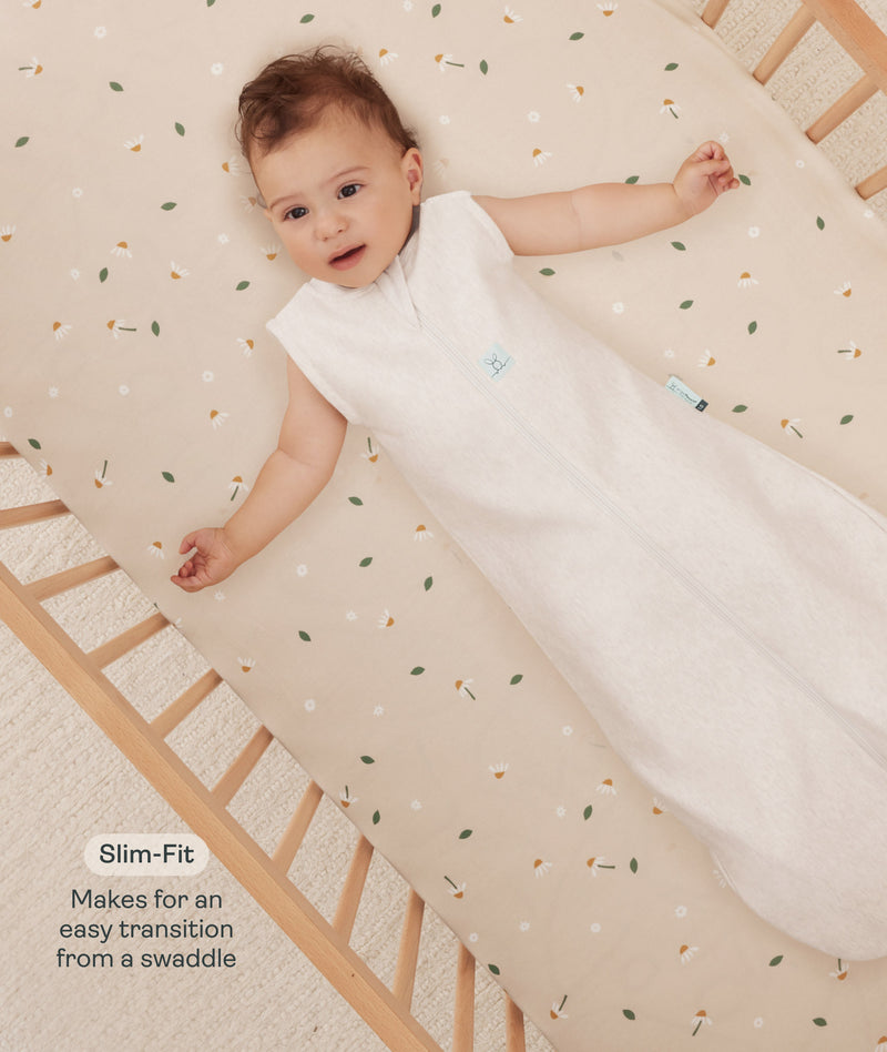 Infant lying in a wooden crib wearing a sleeveless Sleep Sack in Oatmeal Marle with text highlighting slim fit design for easy transition from swaddling.