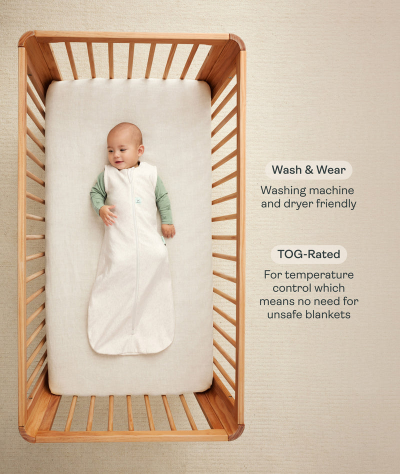 Infant wearing a sleeveless Sleep Sack lying inside a wooden crib with text highlighting wash & wear and TOG rating features.