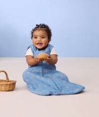 Infant sitting on the floor wearing ergoPouch Sleep Sack 0.2 TOG in Petit Pretzel and holding a fake pretzel toy