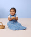 Infant sitting on the floor wearing ergoPouch Sleep Sack 0.2 TOG in Petit Pretzel and holding a fake pretzel toy