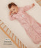 Infant lying in a wooden crib wearing a pink floral sleeved sleep sack with text highlighting slim fit design for an easy transition from swaddling.