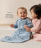 Two babies wearing long-sleeved sleep sacks sit on a carpet with text highlighting slim-fit design for an easy transition from swaddling.
