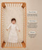 Smiling infant lying in a wooden crib wearing a long-sleeved sleep sack, with text highlighting wash & wear, TOG rating, and sleeve features.