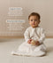Infant sitting, wearing a sleeved Sleep Sack 1.0 TOG Oatmeal Marle, while holding a wooden toy. Text highlighting organic cotton and stretchy-bell-shaped design.