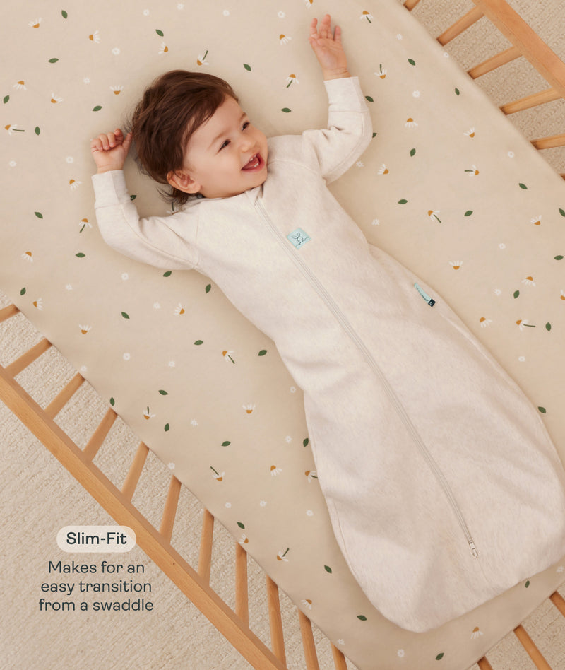 Infant lying in a wooden crib wearing a a long-sleeved Sleep Sack in Oatmeal Marle with text highlighting slim fit design for easy transition from swaddling.