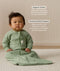 Infant sitting on a white mat, wearing a Sleeved Sleep Sack 1.0 TOG Willow with text overlay highlighting organic cotton and stretchy & bell-shaped design.