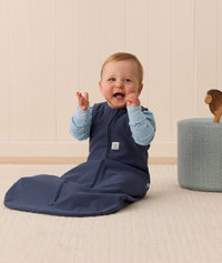 Infant in an ergoPouch Sleep Sack 1.0 TOG Ink sitting on a light wooden floor with a neutral wall background.