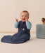 Infant in an ergoPouch Sleep Sack 1.0 TOG Ink sitting on a light wooden floor with a neutral wall background.
