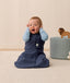 Infant in an ergoPouch Sleep Sack 1.0 TOG Ink sitting on a light wooden floor with a neutral wall background.