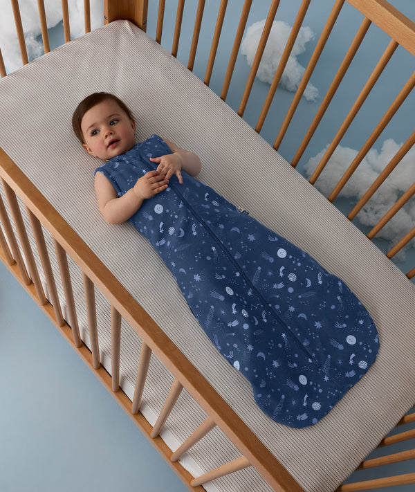 Baby lying in a crib wearing an ergoPouch Sleep Sack 1.0 TOG Starbeam 