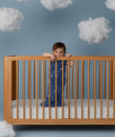 Child standing in a wooden crib wearing an ergoPouch Sleep Sack 1.0 TOG Starbeam