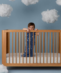 Child standing in a wooden crib wearing an ergoPouch Sleep Sack 1.0 TOG Starbeam