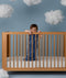 Child standing in a wooden crib wearing an ergoPouch Sleep Sack 1.0 TOG Starbeam
