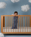 Child standing in a wooden crib wearing an ergoPouch Sleep Sack 1.0 TOG Starbeam