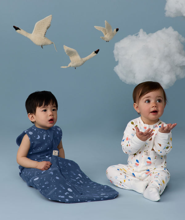 Two infants sitting in ergoPouch sleepwear, one in a Sleep Sack 1.0 TOG Starbeam, the other in a Long Sleeve Romper 1.0 TOG Daydream.