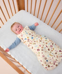 Smiling infant in a crib wearing ergoPouch Sleeping Sack 2.5 TOG Bon Appetit, a warm sleeping bag
