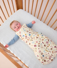Smiling infant in a crib wearing ergoPouch Sleeping Sack 2.5 TOG Bon Appetit, a warm sleeping bag