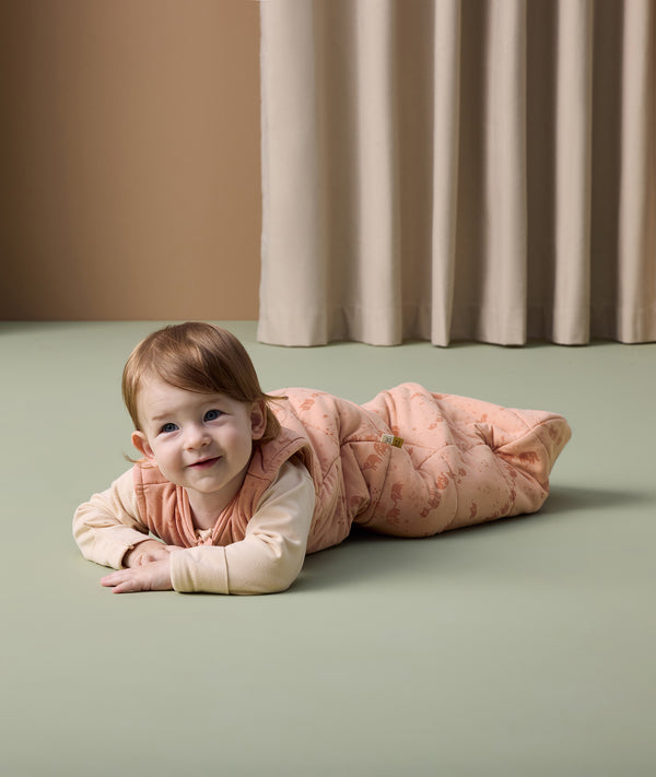 A smiling baby lying on its stomach wearing ergoPouch Sleep Sack 2.5 TOG in Elephant Parade