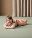 A smiling baby lying on its stomach wearing ergoPouch Sleep Sack 2.5 TOG in Elephant Parade
