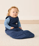 An infant sitting, wearing an ergoPouch Sleep Sack 2.5 TOG Ink over a long sleeve romper.