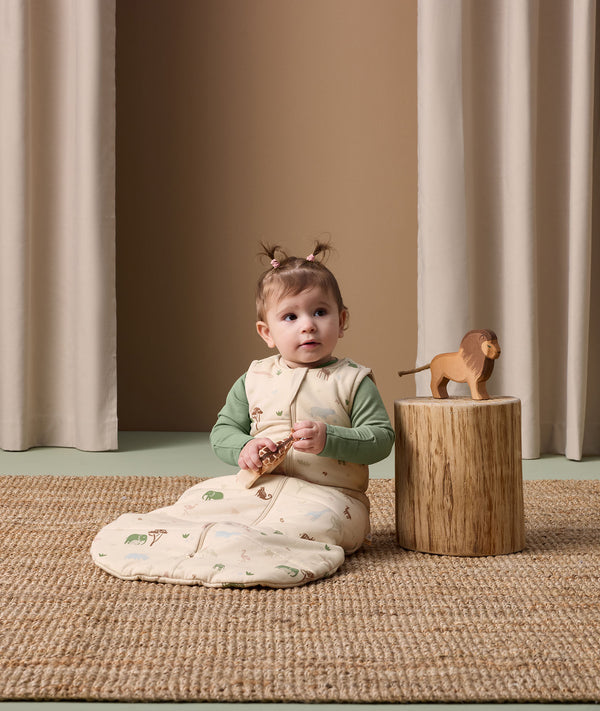 Baby sitting in ergoPouch Sleep Sack Savannah, holding animal toy