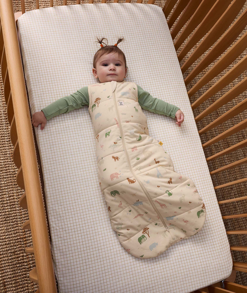 Baby wearing ergoPouch Sleep Sack 2.5 TOG Savannah over a Long Sleeve Romper, lying in a cot