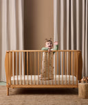 A baby standing in a wooden crib wearing ergoPouch Sleep Sack with cute animal prints
