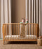 A baby standing in a wooden crib wearing ergoPouch Sleep Sack with cute animal prints