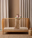A baby standing in a wooden crib wearing ergoPouch Sleep Sack with cute animal prints