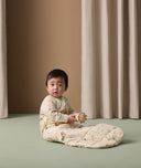 Infant wearing ergoPouch Sleep Sack with Sleeves in Savannah print, sitting on the floor while holding a toy.