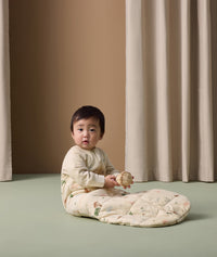 Infant wearing ergoPouch Sleep Sack with Sleeves in Savannah print, sitting on the floor while holding a toy.
