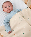Baby lying under a ergoPouch HugMe Blanket in Daisy Sprinkle and looking at the camera