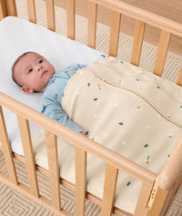 Baby lying arms out under a ergoPouch HugMe Blanket in Daisy Sprinkle