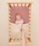 Baby lying in a bassinet under an ergoPouch HugMe Blanket in Daisy Sprinkle